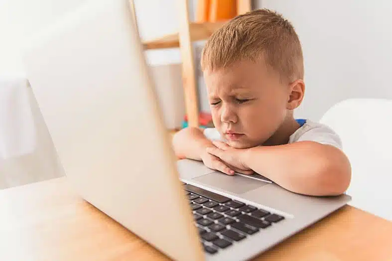 Young boy resting his head on a laptop looking bored