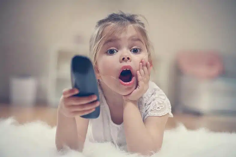Young girl lying on the floor watching TV with a remote in her hand