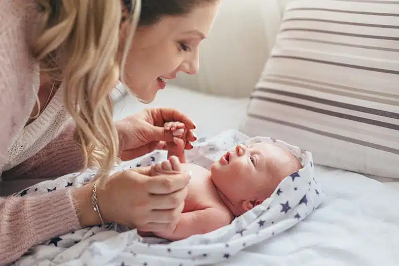 Mother playing with her newborn baby on a bed