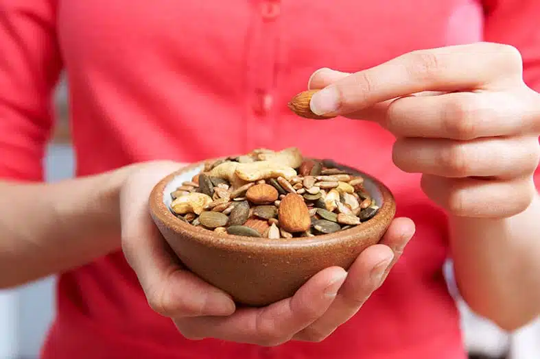 Person holding a small bowl of mixed nuts and seeds