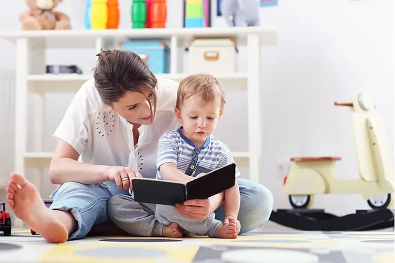 Mother reading a picture book with her toddler on a playroom floor