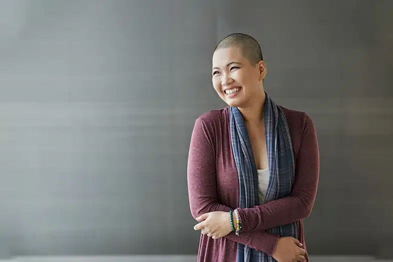 Smiling woman with a shaved head standing against a plain wall