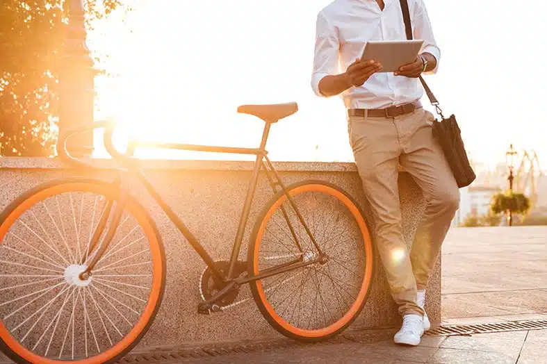Commuter with a tablet leaning against a bicycle at sunset