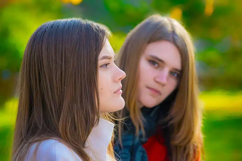 Two teenage girls sitting together outdoors, one turned away