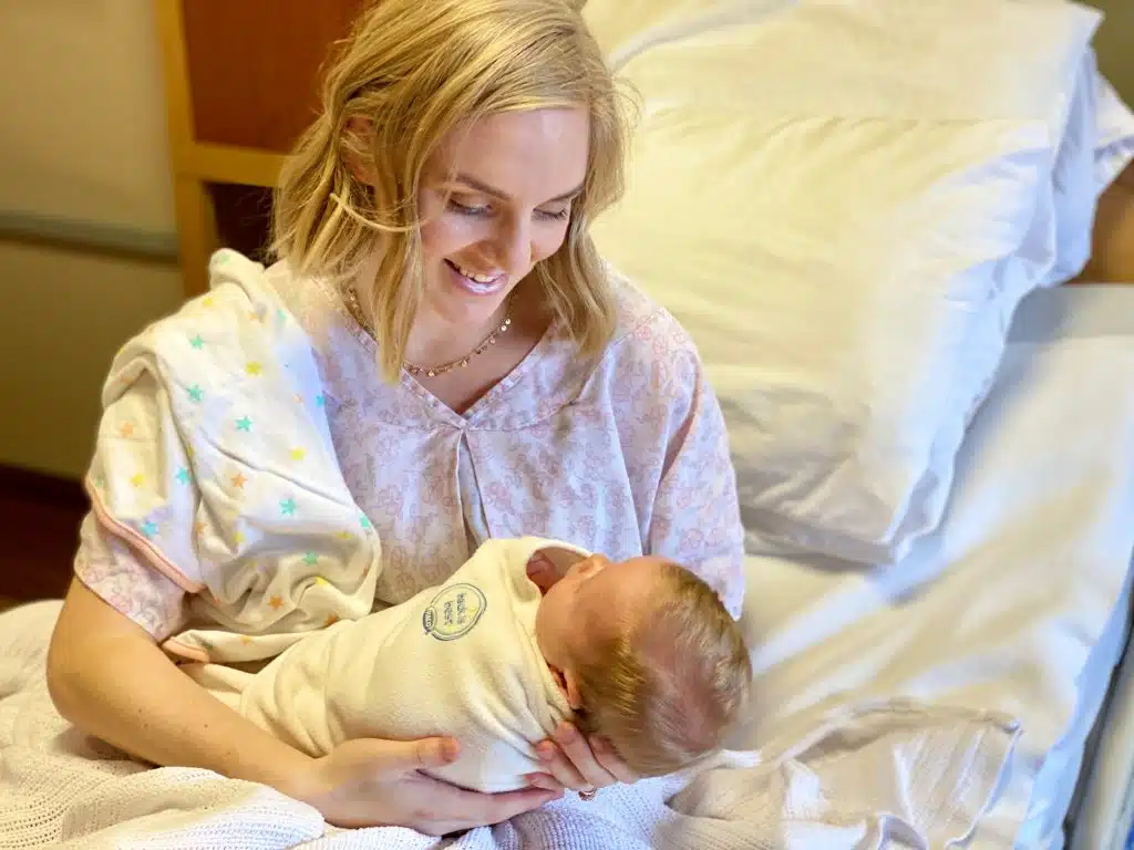 New mother holding her swaddled newborn in a hospital bed