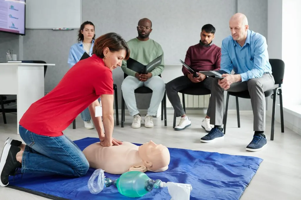 Instructor demonstrating CPR chest compressions on a manikin to a class