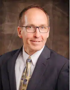 Madisonhealth staff portrait: man with glasses in a navy suit and patterned tie