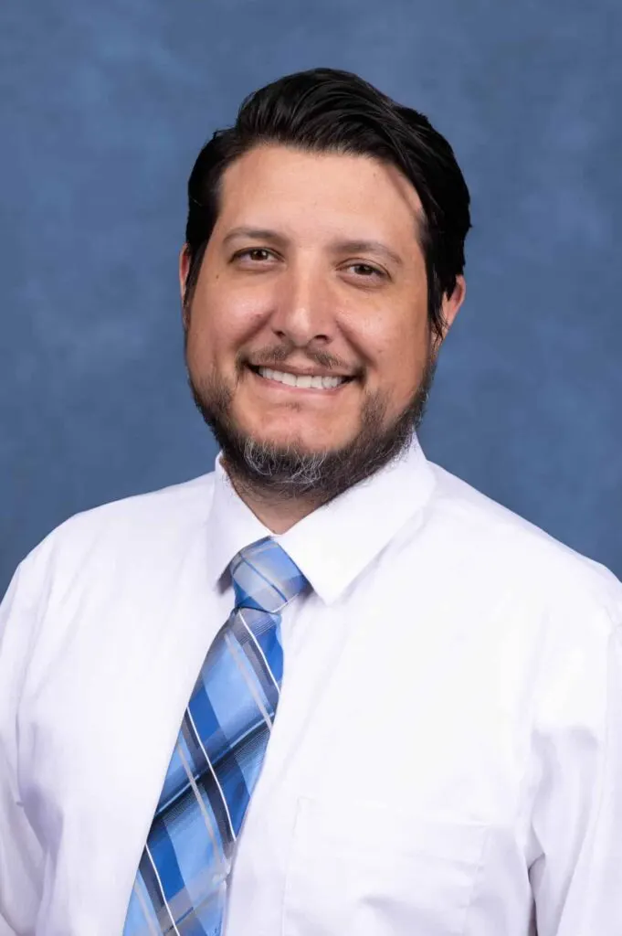 Madisonhealth staff portrait: man in a white shirt and blue plaid tie, blue backdrop