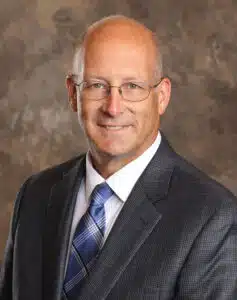 Madisonhealth staff portrait: man with glasses in a dark suit and plaid tie