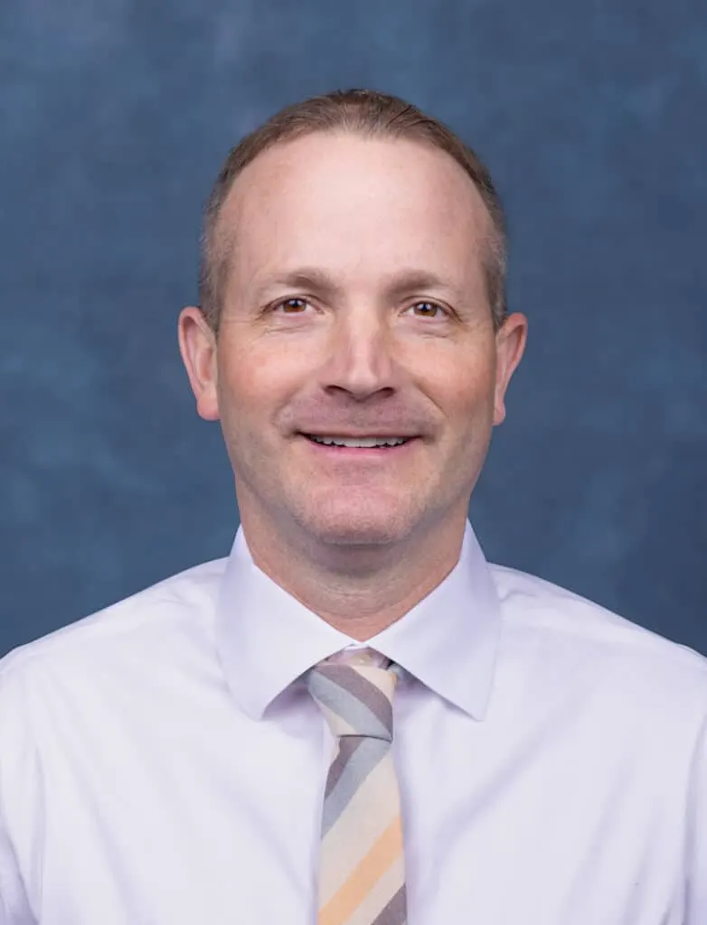 Matheau Eysser, smiling in a dress shirt and striped tie, against a blue studio backdrop