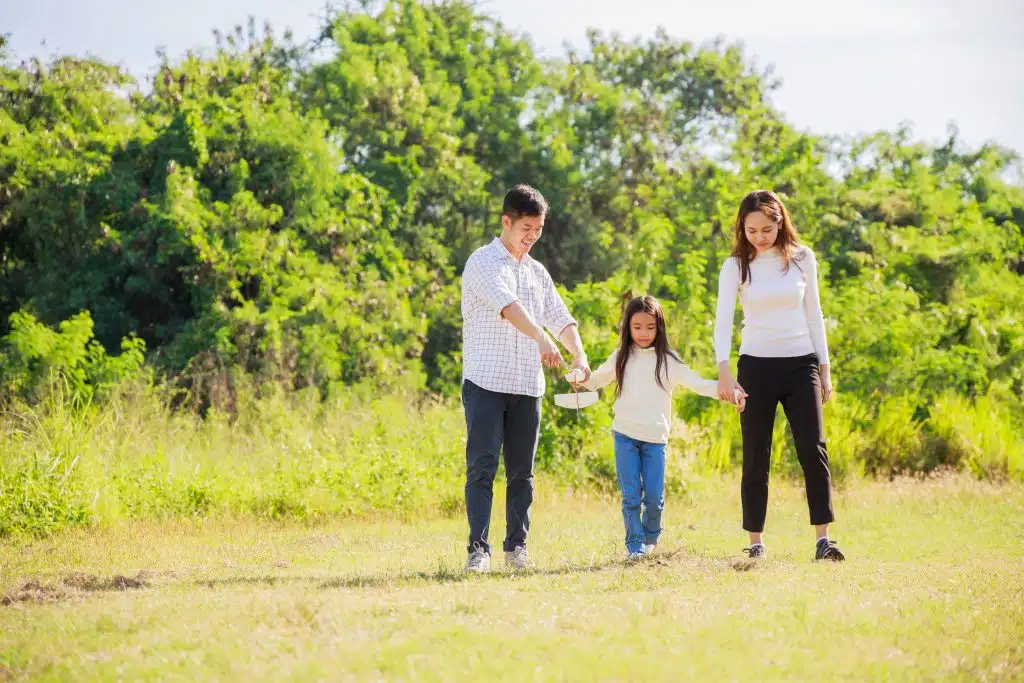 Family of three walking hand in hand across a sunny meadow