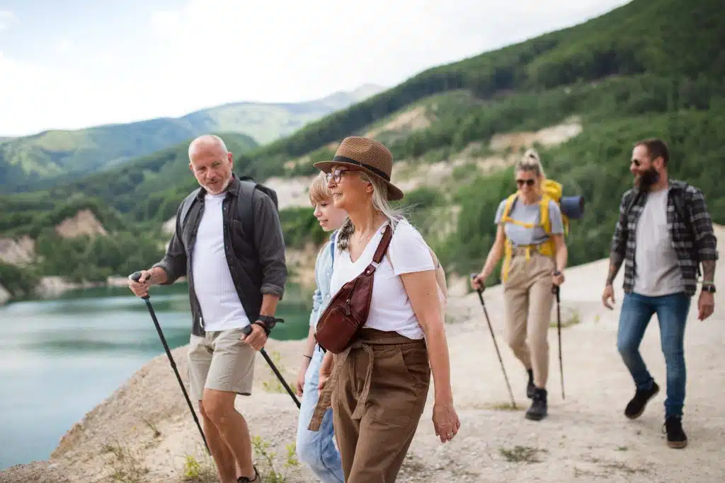 Group of friends hiking with poles along the shore of a mountain lake