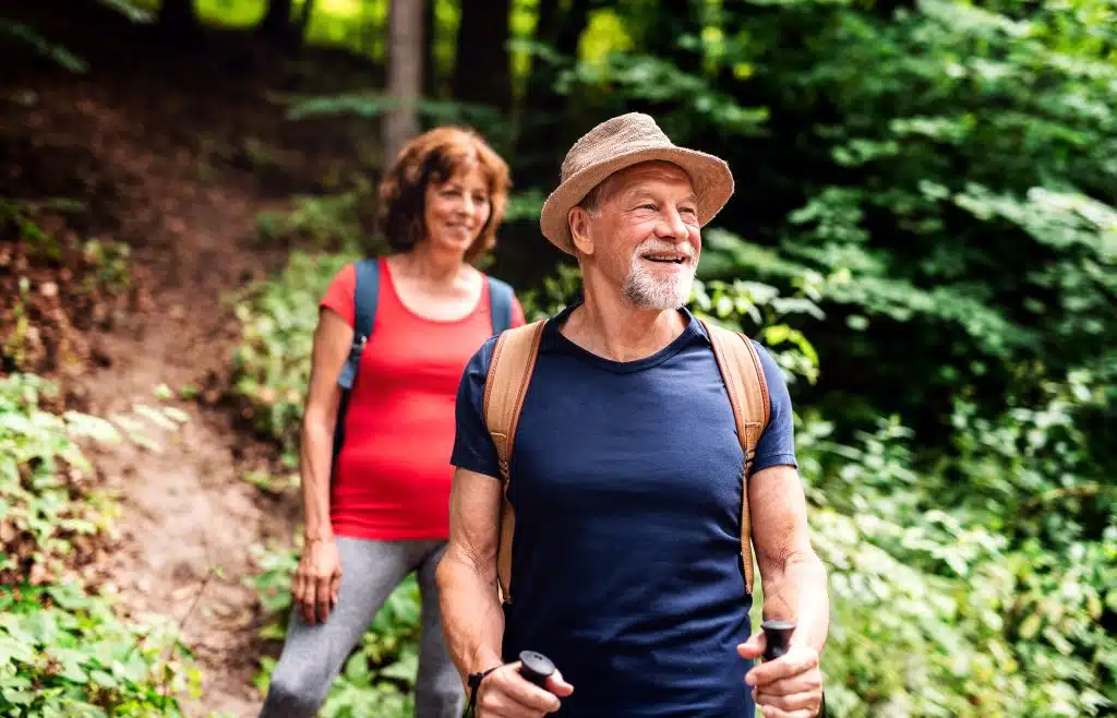 Older couple hiking a wooded trail with walking poles