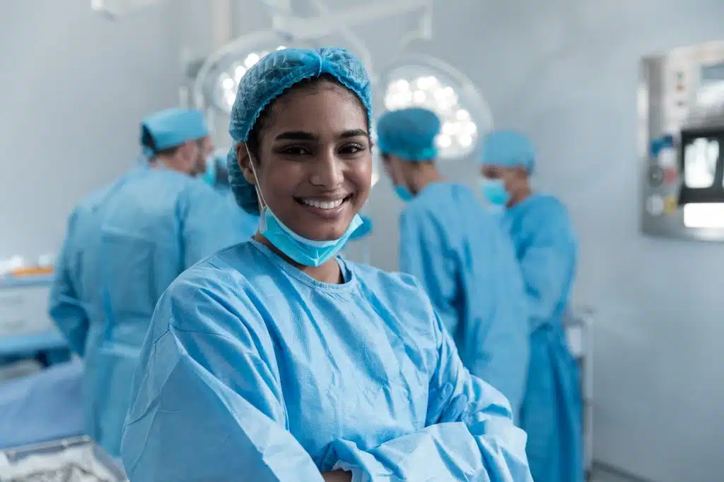 Smiling surgeon in blue scrubs and cap with the surgical team working behind her