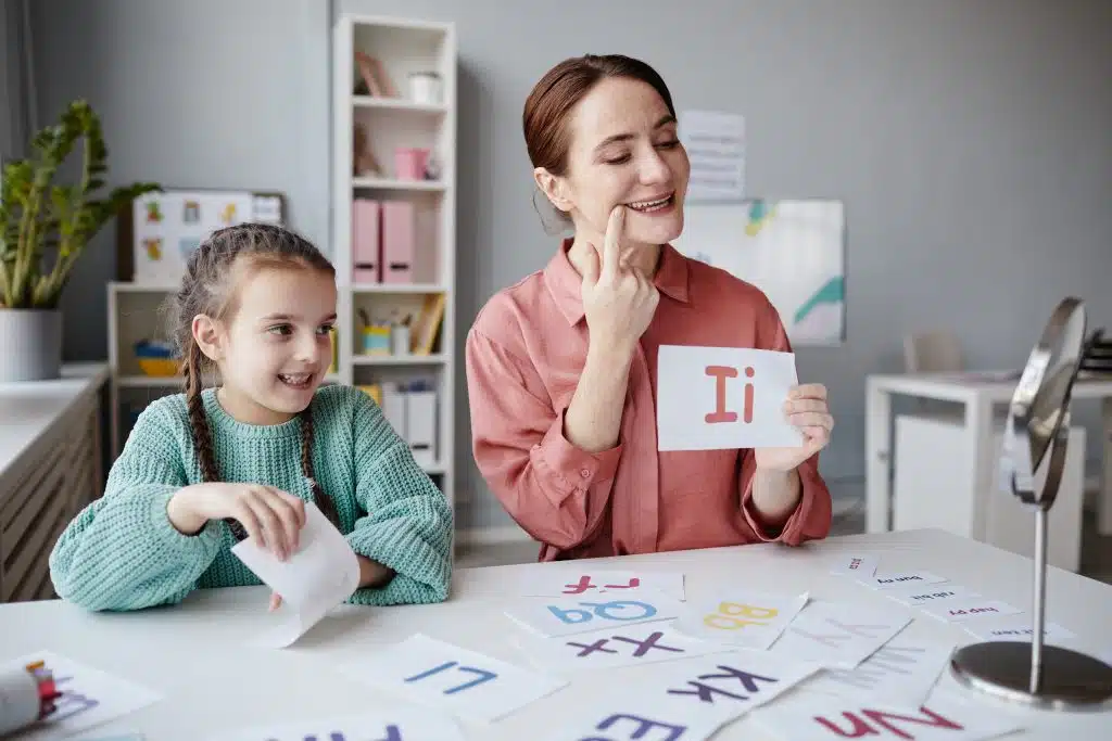 Speech therapist holding up a letter card during a session with a young girl