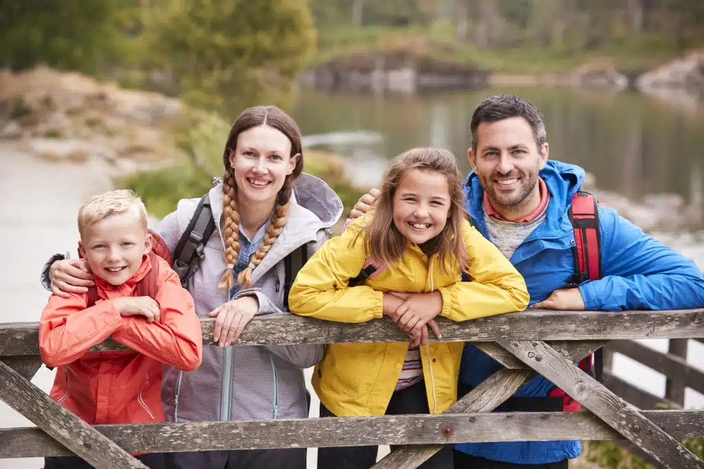 Family of four in rain jackets leaning on a gate beside a lake