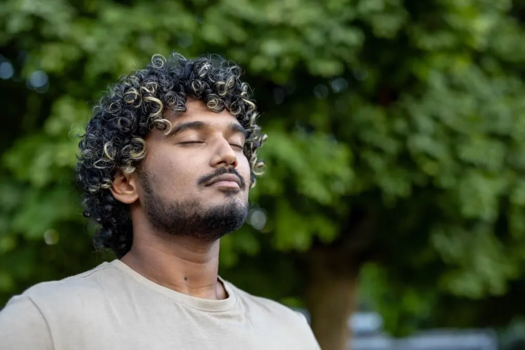 Man standing outdoors with his eyes closed, breathing slowly to calm down