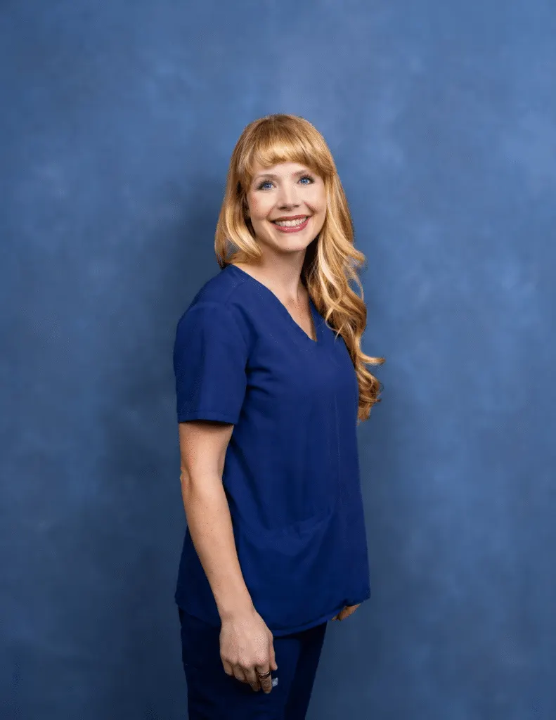 Madisonhealth staff portrait: woman with long red hair in navy scrubs, blue backdrop