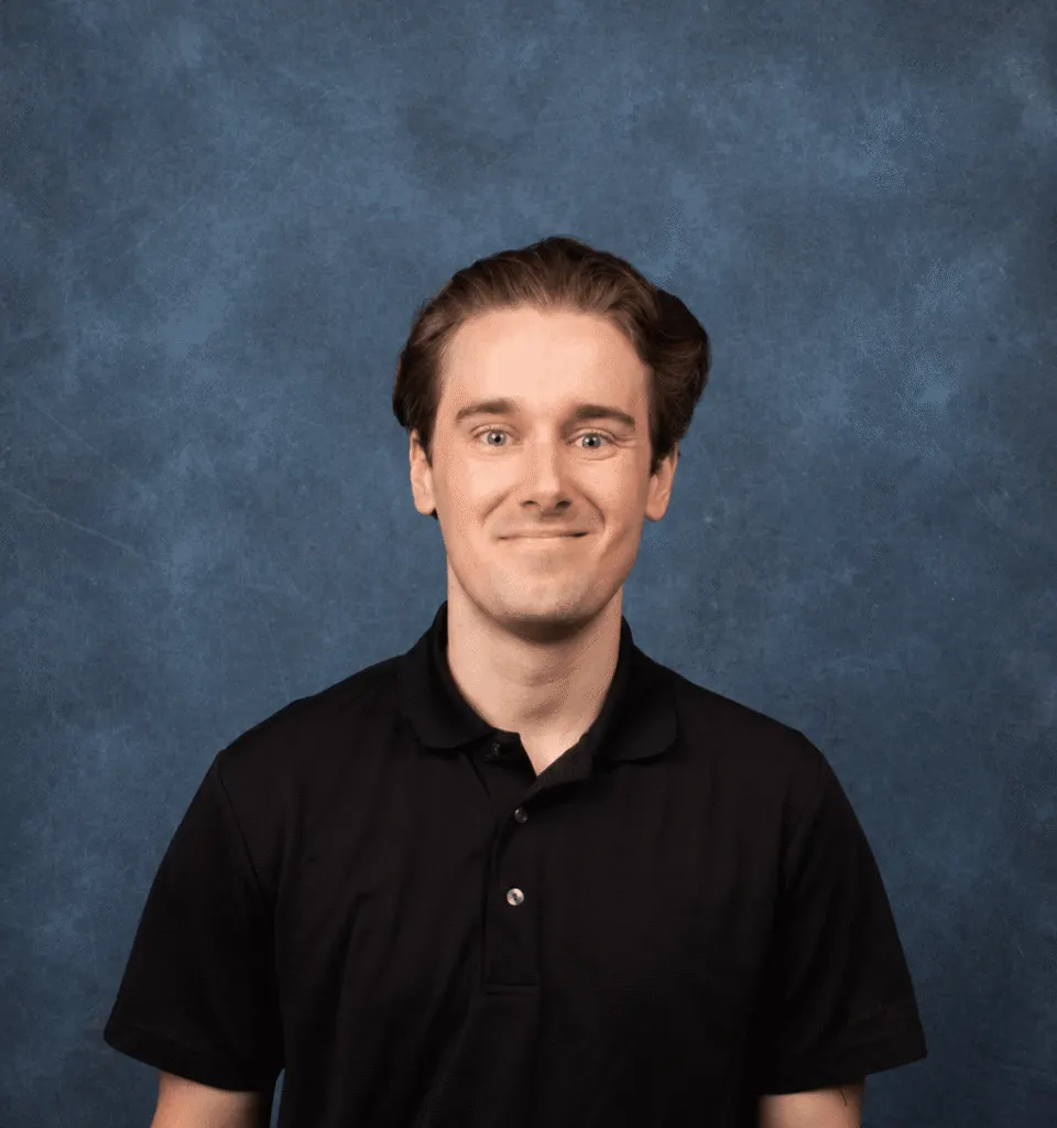 Madisonhealth staff portrait: young man in a black polo shirt against a blue backdrop