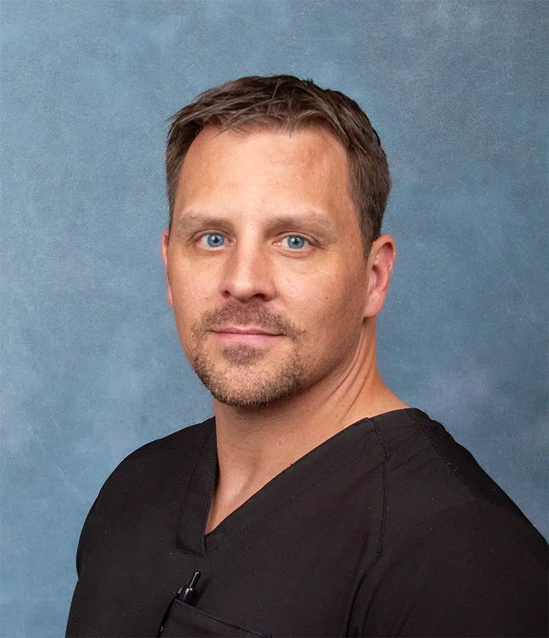 Eric Jensen, hospitalist physician at Madisonhealth, in black scrubs against a blue backdrop
