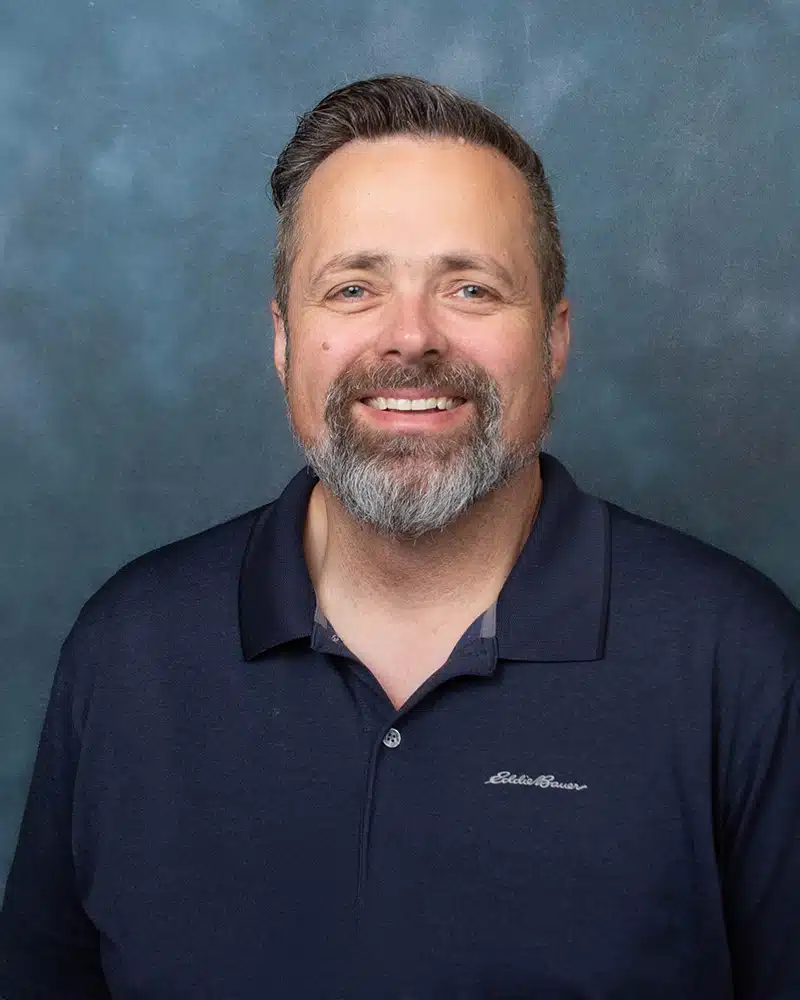 Madisonhealth staff portrait: bearded man in a navy polo shirt against a blue backdrop