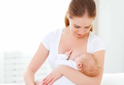 mother breastfeeding her newborn baby in a white bed